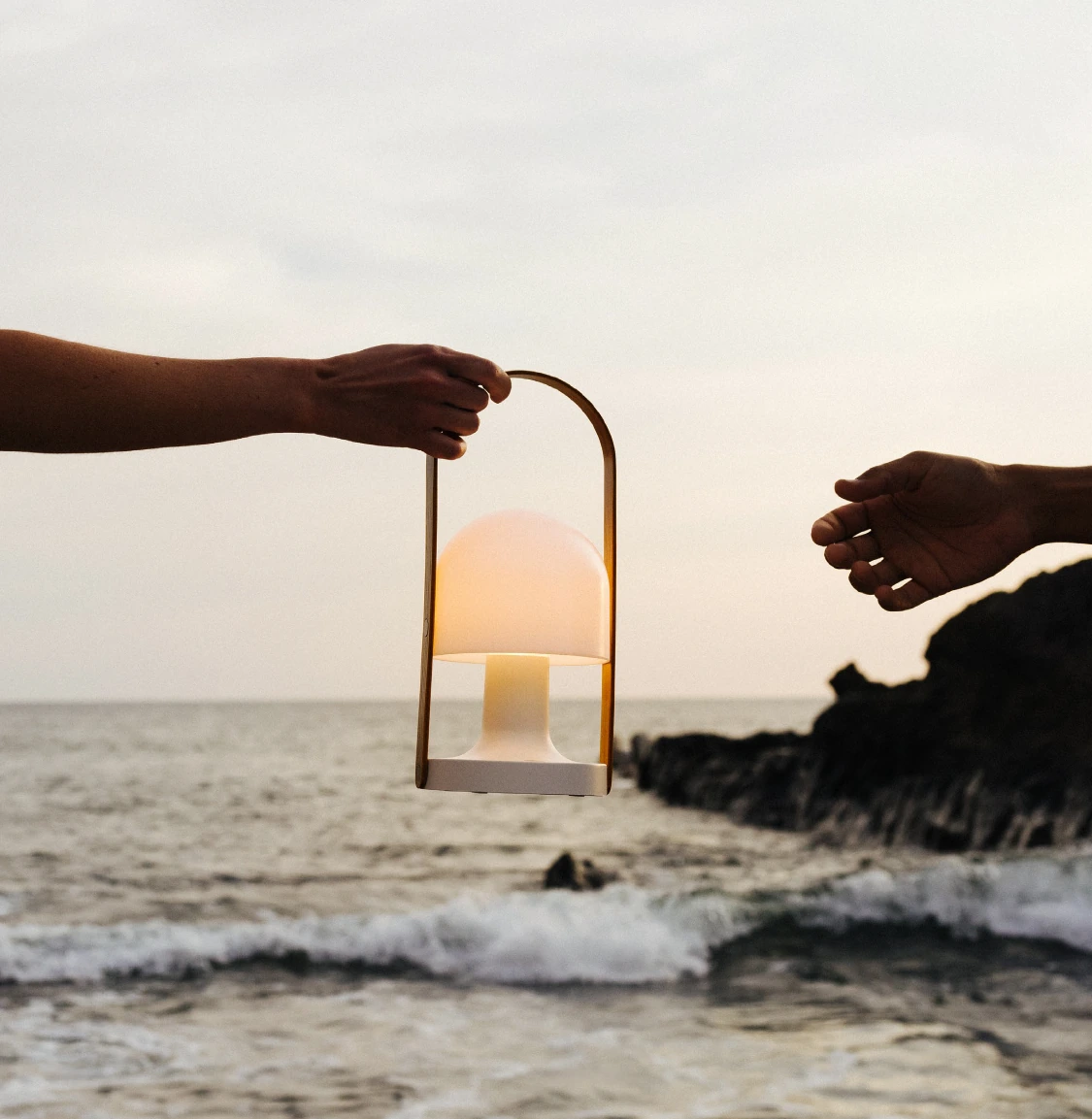 Two hands passing a portable luminaire above the shoreline during a product experience