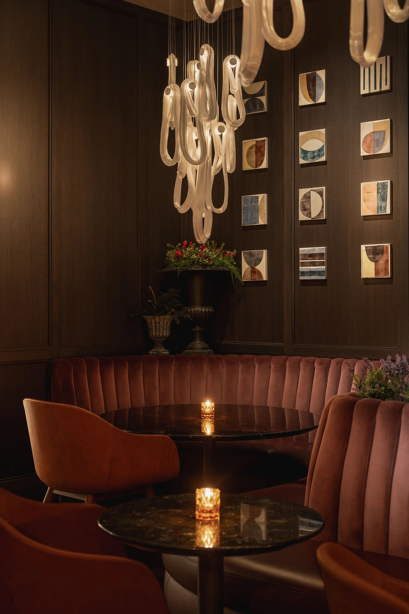 Hotel lounge bar with sculptural glass pendant cluster over velvet banquettes